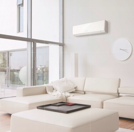 Klimatyzator ścienny w jasnym salonie z narożną sofą, dużym oknem i minimalistycznym zegarem.