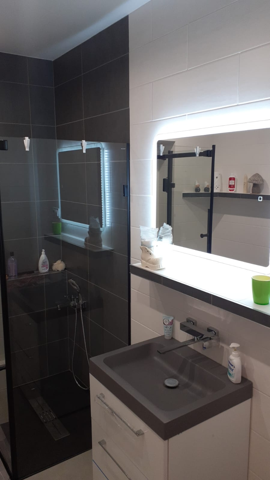 Nowoczesna łazienka z ciemnoszarą kabiną prysznicową typu walk-in, umywalką w kolorze grafitu i podświetlanym lustrem.