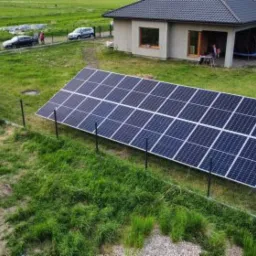 Panel słoneczny na trawniku przed domem jednorodzinnym, widok z góry, ogrodzenie z siatki.
