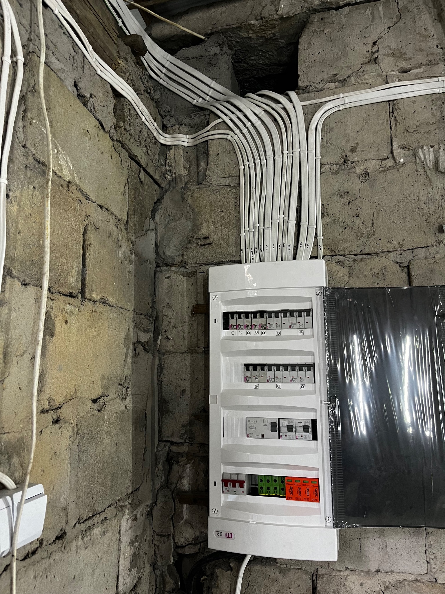 Nowa skrzynka z bezpiecznikami i liczne przewody elektryczne zamontowane na surowej, kamiennej ścianie w Daleszycach.