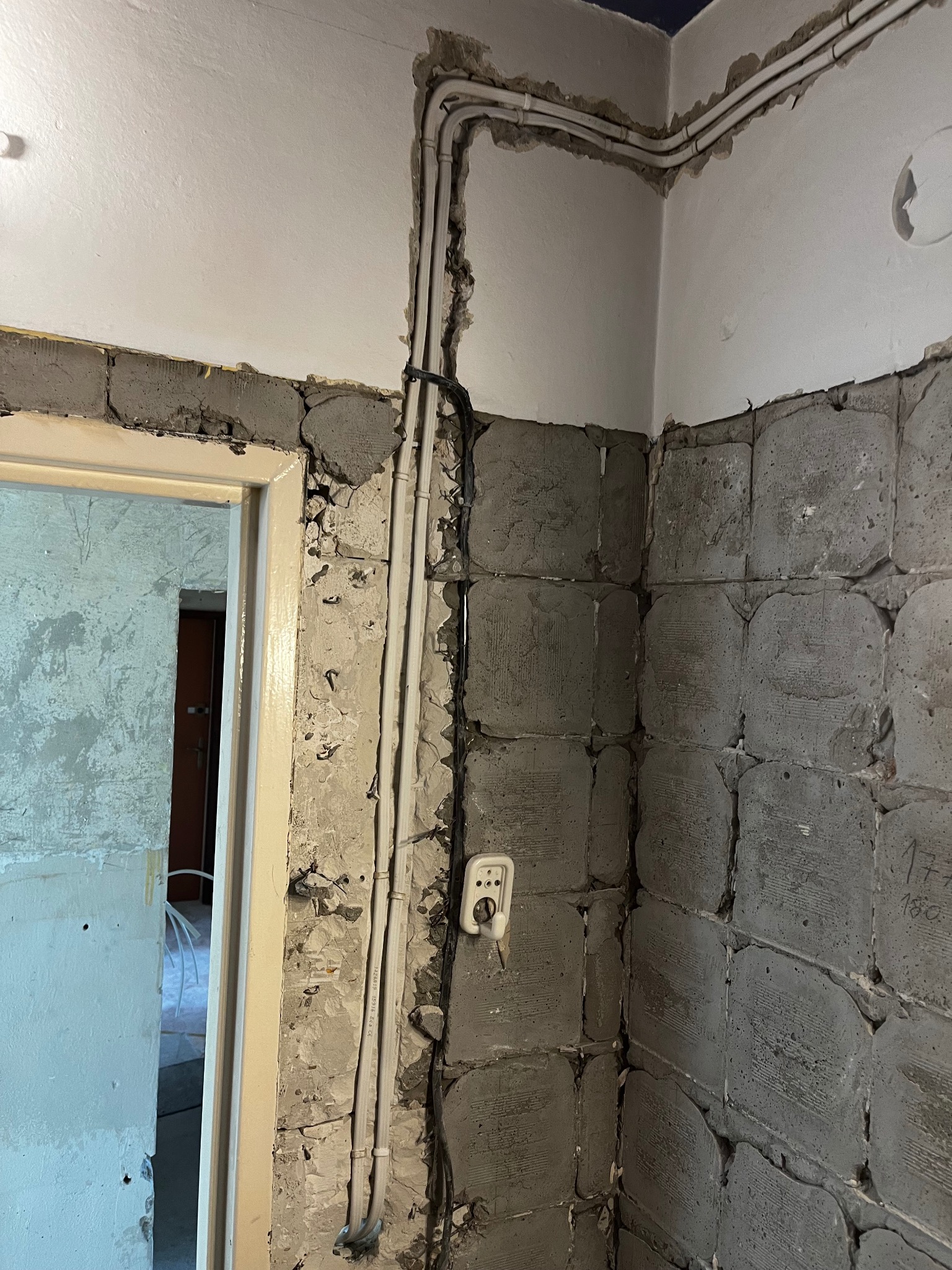 Wewnętrzne ściany w trakcie remontu z widocznymi przewodami elektrycznymi i gniazdkiem, surowy stan wykończenia.