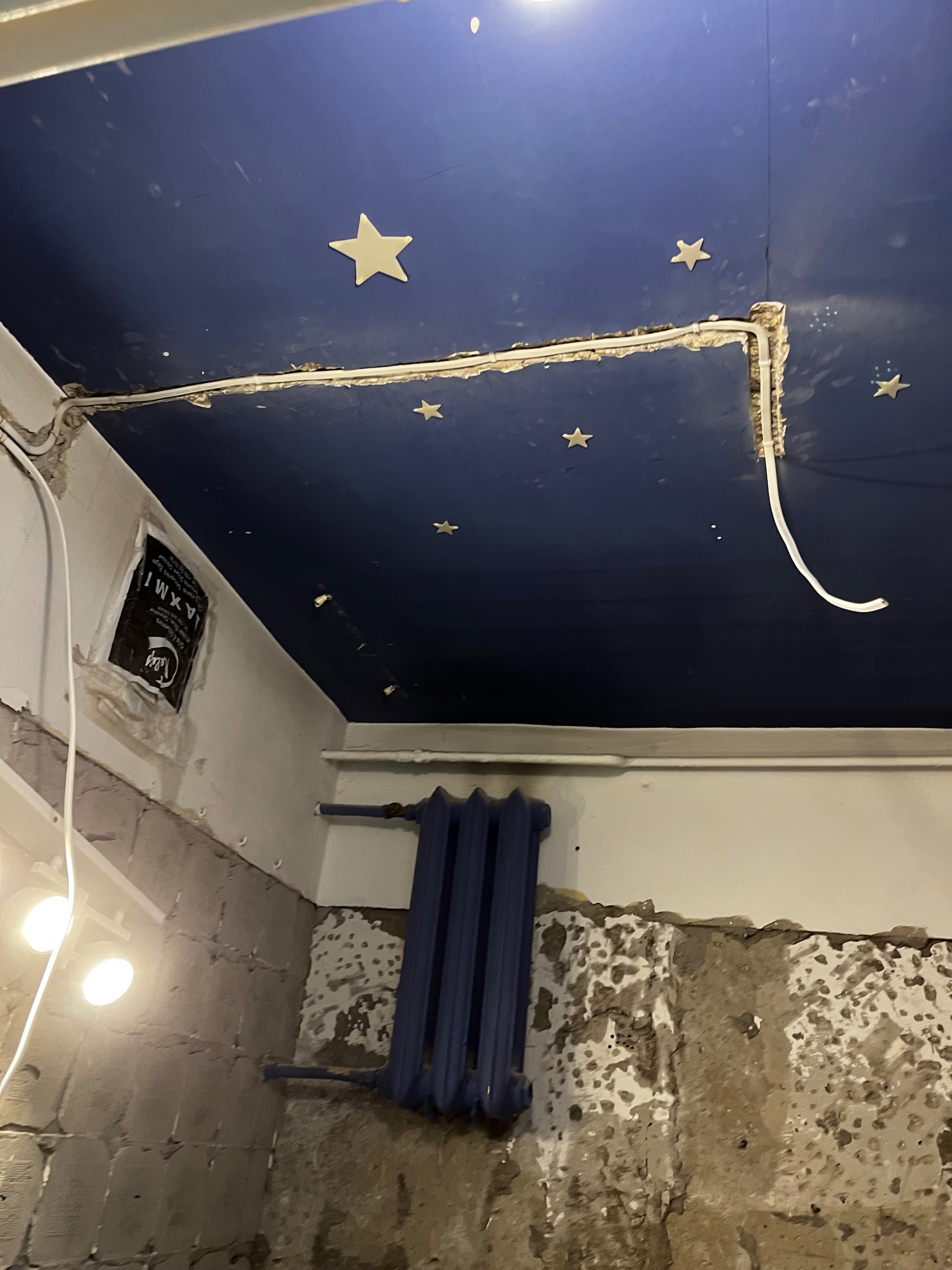 Niedokończona instalacja elektryczna pod sufitem z dekoracjami w kształcie gwiazd, widoczne kable i fragment ściany z grzejnikiem.