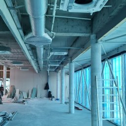 INSTALTOR, instaltor.pl - Wnętrze w trakcie instalacji systemu wentylacyjnego z widocznymi kanałami wentylacyjnymi owiniętymi folią aluminiową i jednostką centralną pod sufitem. Na podłodze widoczne materiały budowlane...