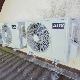 INSTALTOR, instaltor.pl - Cztery jednostki zewnętrzne klimatyzacji marki AUX zamontowane na elewacji budynku, widoczne z perspektywy dachu.