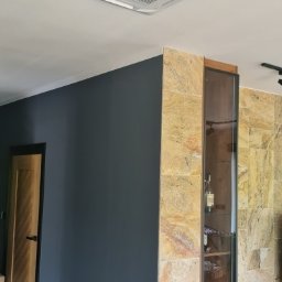 INSTALTOR, instaltor.pl - Kasetonowa jednostka klimatyzacyjna zamontowana w suficie podwieszanym, widoczna w nowoczesnym wnętrzu z ciemnoszarą ścianą i elementami wykończenia z kamienia.