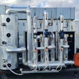 INSTALTOR, instaltor.pl - Instalacja przemysłowa na dachu budynku z rurami, zbiornikami i wentylacją w srebrnej izolacji, widoczne manometry i pompy.