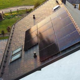 KLABAR - Widok z góry na dach domu z zainstalowanymi panelami słonecznymi, brązowa dachówka, widoczny fragment ogrodu z dwoma osobami.