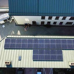 KLABAR - Widok z góry na budynek z panelami słonecznymi na dachu, na dziedzińcu zaparkowany biały samochód dostawczy z otwartymi drzwiami i grupa osób w pobliżu wejścia do budynku.