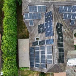 KLABAR - Widok z drona na dom z zamontowanymi panelami fotowoltaicznymi na dachu, obok zaparkowany biały bus z otwartymi drzwiami