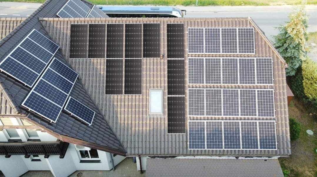 Widok z góry na dach domu z zainstalowanymi panelami słonecznymi o różnych układach i kolorach, z małym oknem dachowym pośrodku.