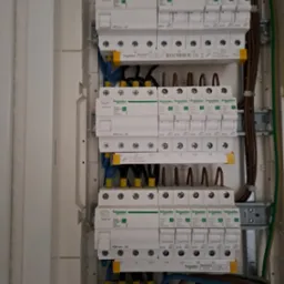 Rozdzielnica elektryczna z zainstalowanymi bezpiecznikami i przewodami, widoczne oznaczenia L1, L2, L3, N oraz logo Schneider Electric na elementach.