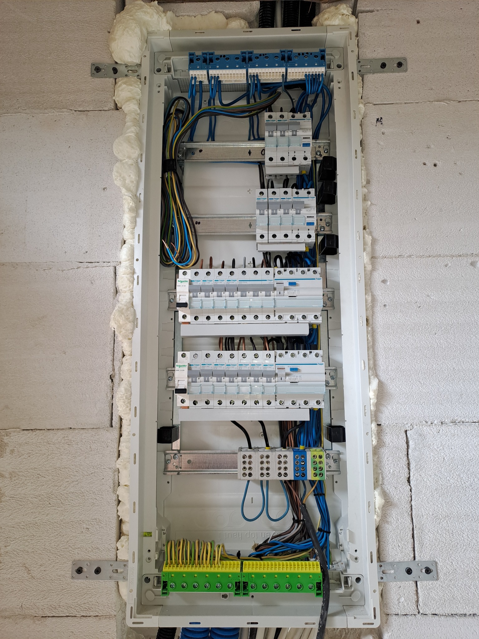 Rozdzielnica elektryczna z zabezpieczeniami i okablowaniem, zamontowana w ścianie z betonu komórkowego, uszczelniona pianką montażową.