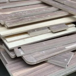 Stos płyt MDF i sklejki z wyfrezowanymi otworami i zaokrąglonymi krawędziami po obróbce CNC, widoczny układ warstw materiału.