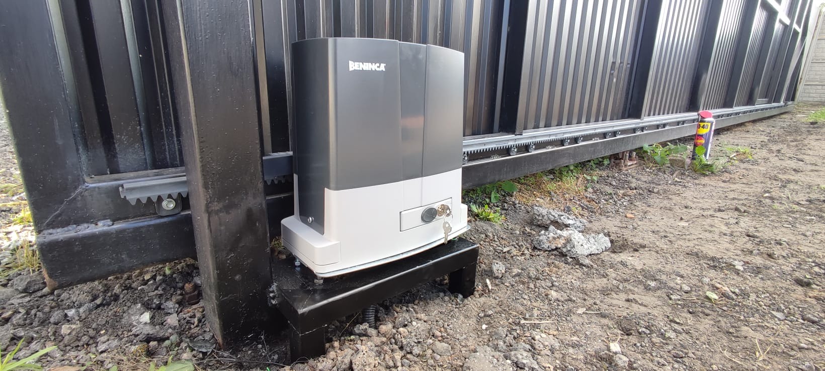 Zamontowany automat do bramy przesuwnej marki Beninca, widoczna listwa zębata, podłoże gruntowe.