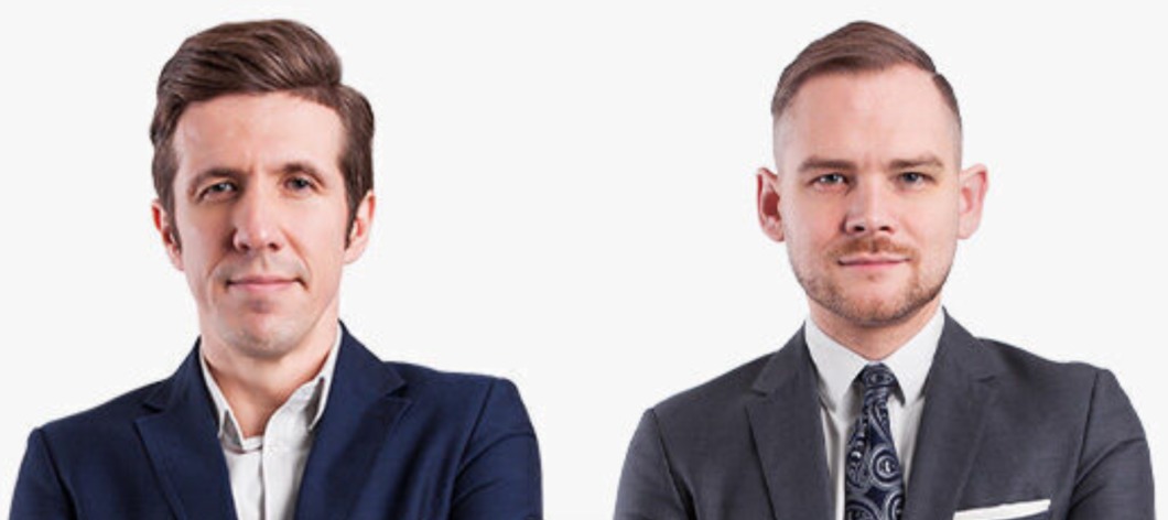 Portret dwóch mężczyzn w garniturach na jasnym tle, jeden w ciemnoniebieskim marynarce i białej koszuli, drugi w szarym garniturze i wzorzystym krawacie.