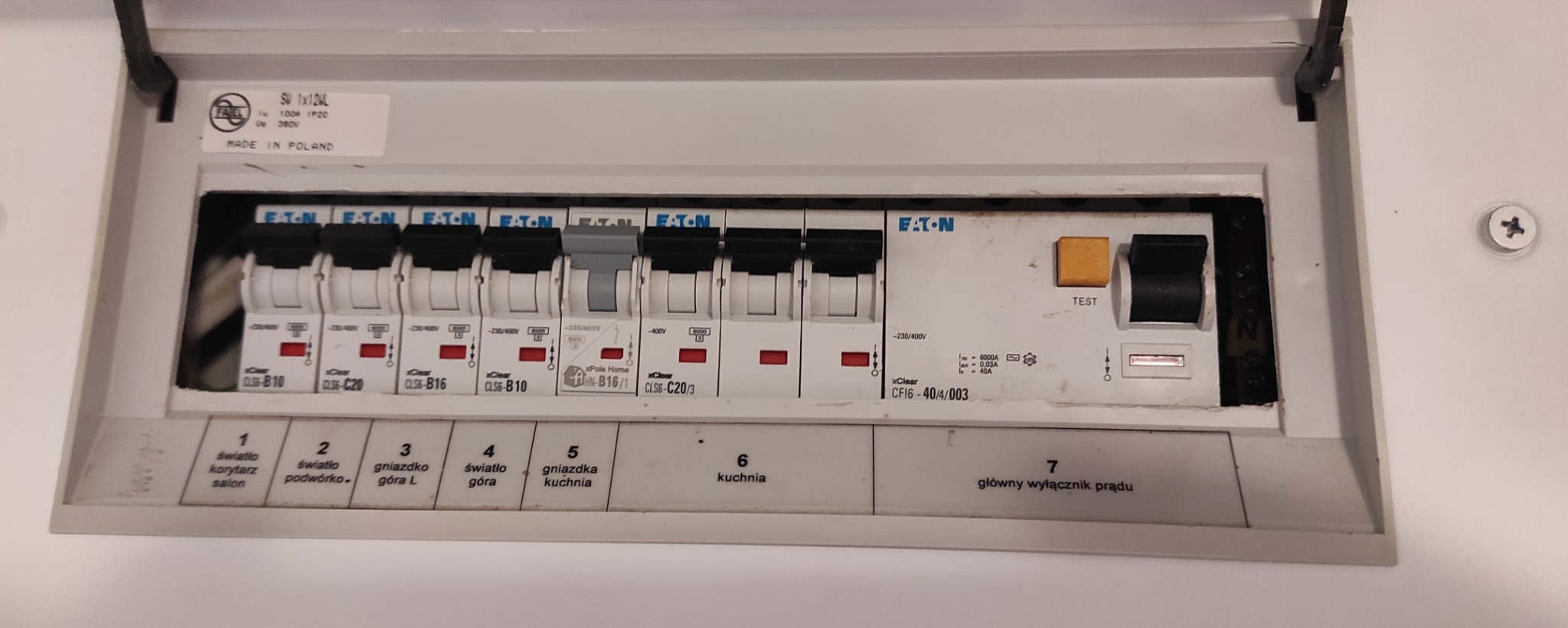 Otwarta skrzynka rozdzielcza z bezpiecznikami marki Eaton, opisane obwody: światło salon, korytarz, podwórko, gniazdko góra L, światło góra, gniazdka kuchnia, kuchnia, główny wyłącznik prądu.