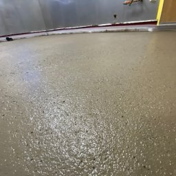 Vanguard Marine - Świeżo wylana, wilgotna posadzka żywiczna w szarym odcieniu, widoczne detale struktury powierzchni i odblaski światła, przy ścianie listwa przypodłogowa.