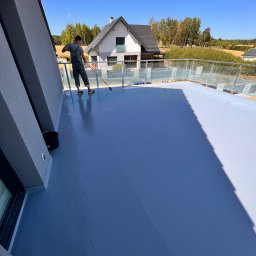 Vanguard Marine - Aplikacja szarej, błyszczącej powłoki na balkonie z szklanymi balustradami; w tle dom jednorodzinny i błękitne niebo.