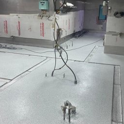 Vanguard Marine - Szara posadzka w hali przemysłowej z widocznymi dylatacjami i sprzętem montażowym, ściany wyłożone płytami ochronnymi.