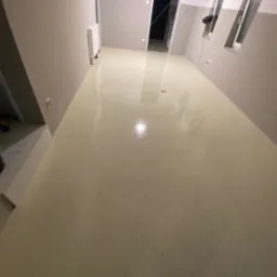 Jasna, jednolita posadzka w odcieniach beżu w pustym pomieszczeniu z szarymi ścianami, widoczne okna i drzwi.