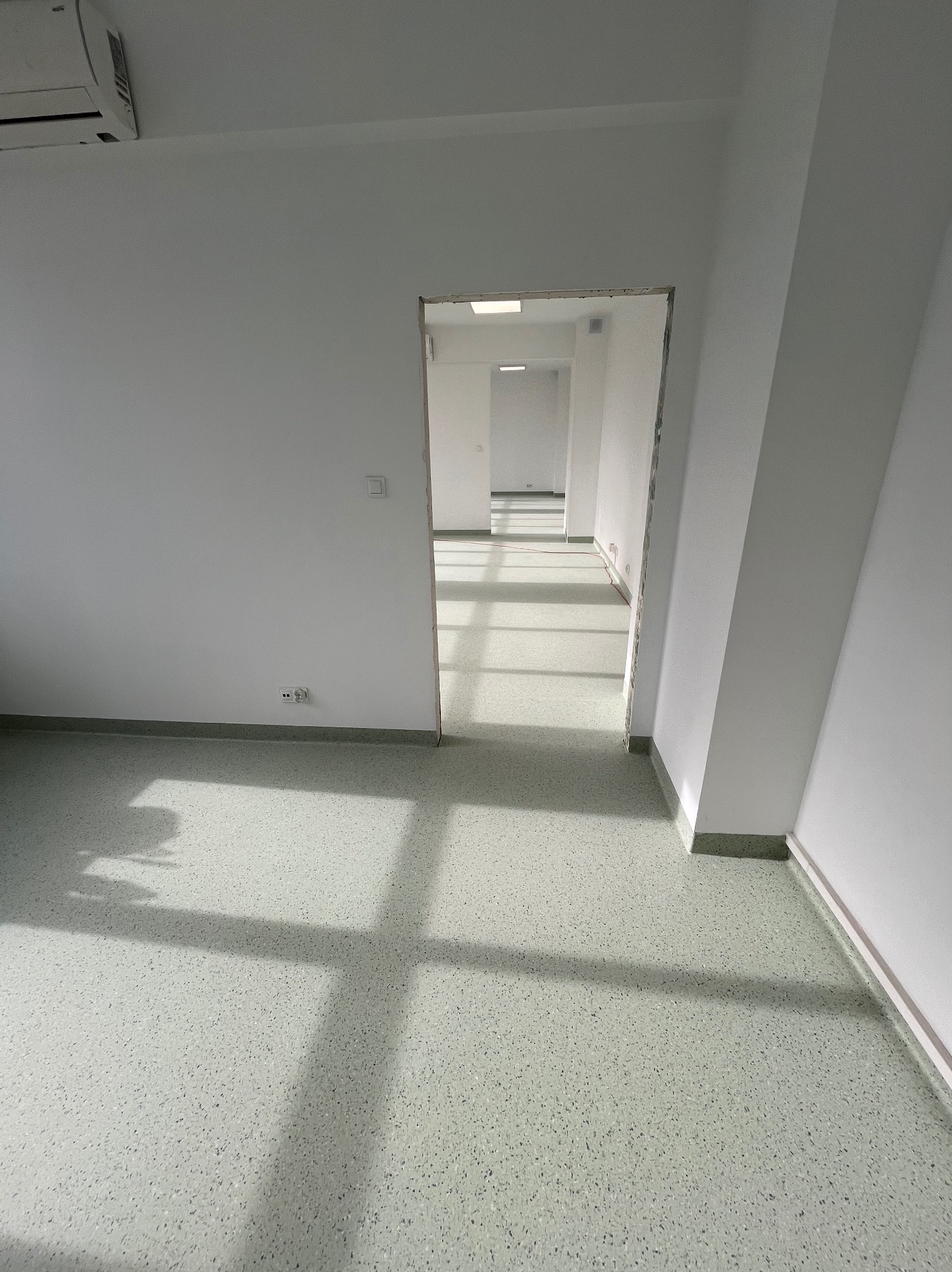 Jasne wnętrze z nową, plamkowaną posadzką i widokiem na długi korytarz z oknami dachowymi, klimatyzator na ścianie.