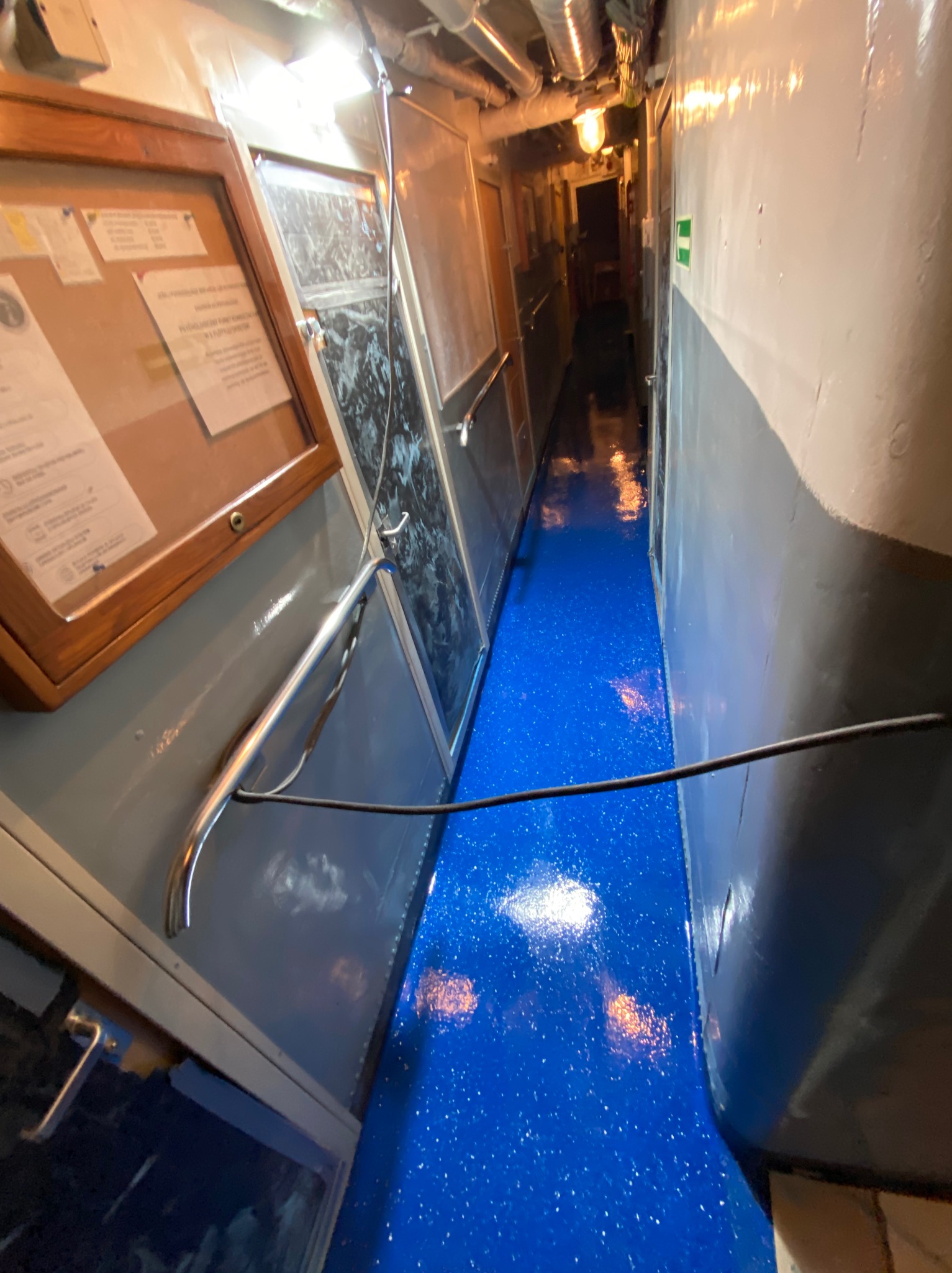 Wnętrze korytarza z błyszczącą, niebieską podłogą z efektem brokatu, szare ściany i metalowe elementy wykończeniowe.