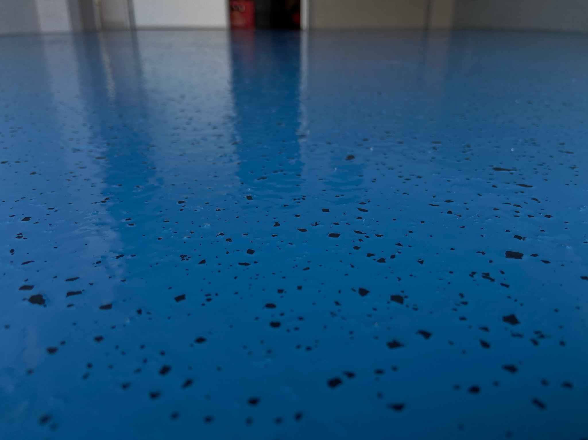 Błyszcząca, błękitna powierzchnia podłogi z ciemnymi drobnymi plamkami, widoczna z niskiej perspektywy, odbijająca światło.