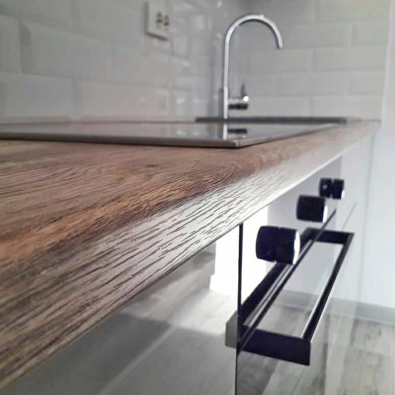 Blat kuchenny z imitacją drewna, wbudowana płyta grzewcza, chromowana bateria i białe kafelki na ścianie w tle.