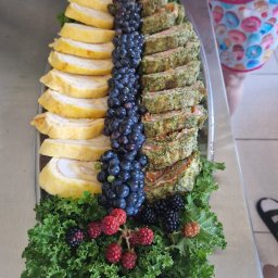 Opus Dorota Kaak - Dekoracyjna taca z roladkami jajecznymi, roladkami z łososia i szpinaku, ciemnymi winogronami, jeżynami i malinami na podkładzie z zielonego jarmużu.