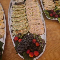 Opus Dorota Kaak - Dwa srebrne półmiski z przekąskami: roladki szpinakowe z łososiem, pasztet z warzywami, sos w metalowej miseczce oraz dekoracja z ciemnych i zielonych winogron, jeżyn i czerwonych śliwek...