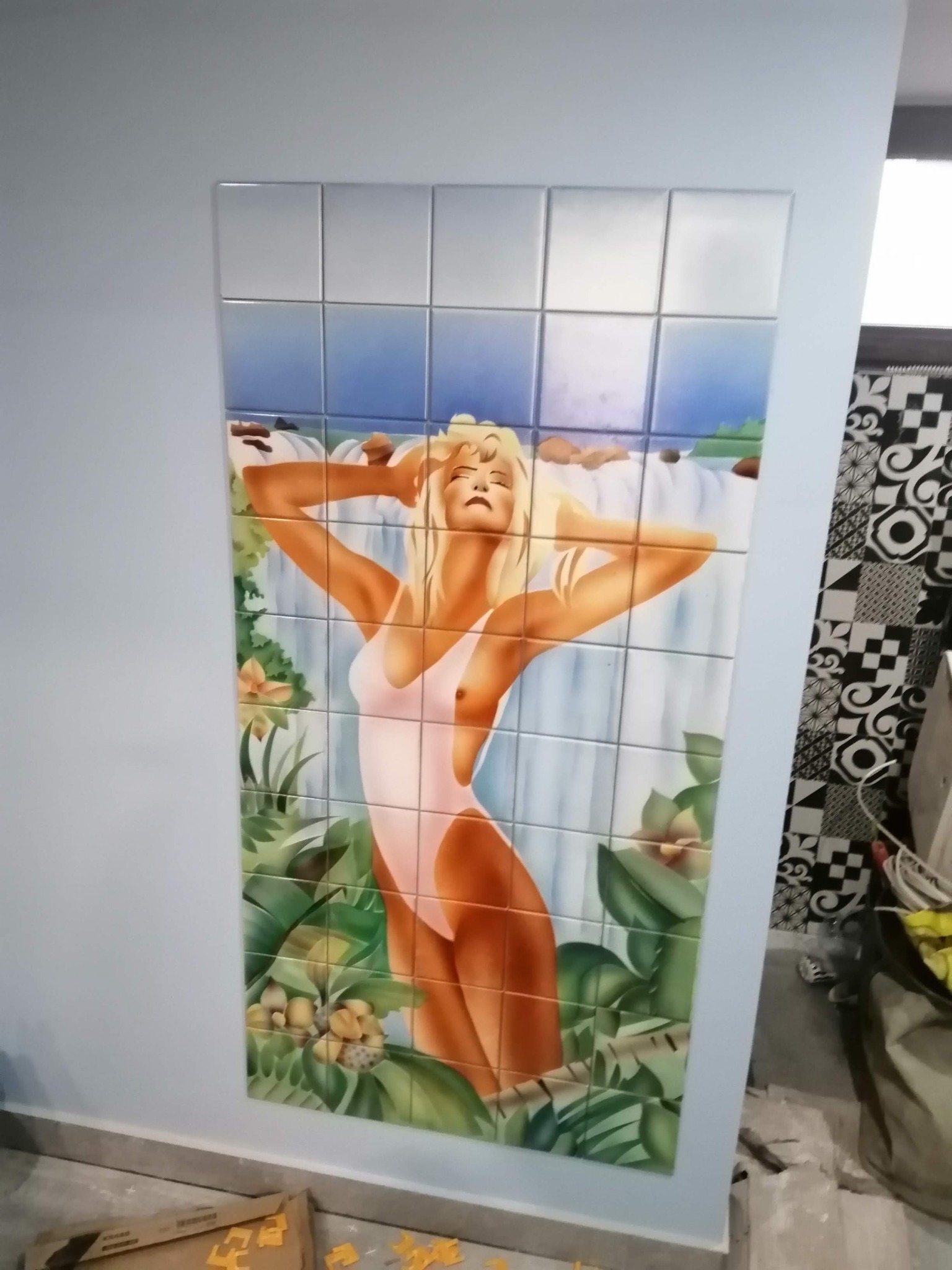 Mozaika ceramiczna przedstawiająca kobietę w stroju kąpielowym na tle wodospadu i tropikalnej roślinności, ułożona na ścianie w łazience.