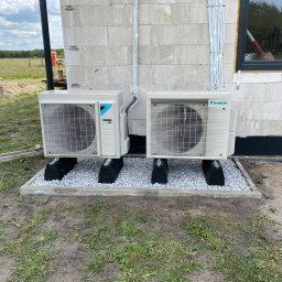 DS Klimatyzacje Daniel Spychała - Dwa klimatyzatory Daikin zamontowane na zewnątrz budynku w Szczecinie, na szarym żwirze. Widoczne przewody prowadzące do wnętrza, ściana z betonu komórkowego.