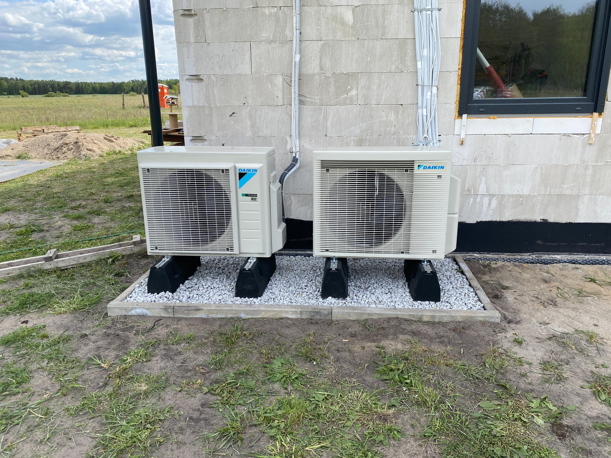 Dwa klimatyzatory Daikin zamontowane na zewnątrz budynku w Szczecinie, na szarym żwirze. Widoczne przewody prowadzące do wnętrza, ściana z betonu komórkowego.