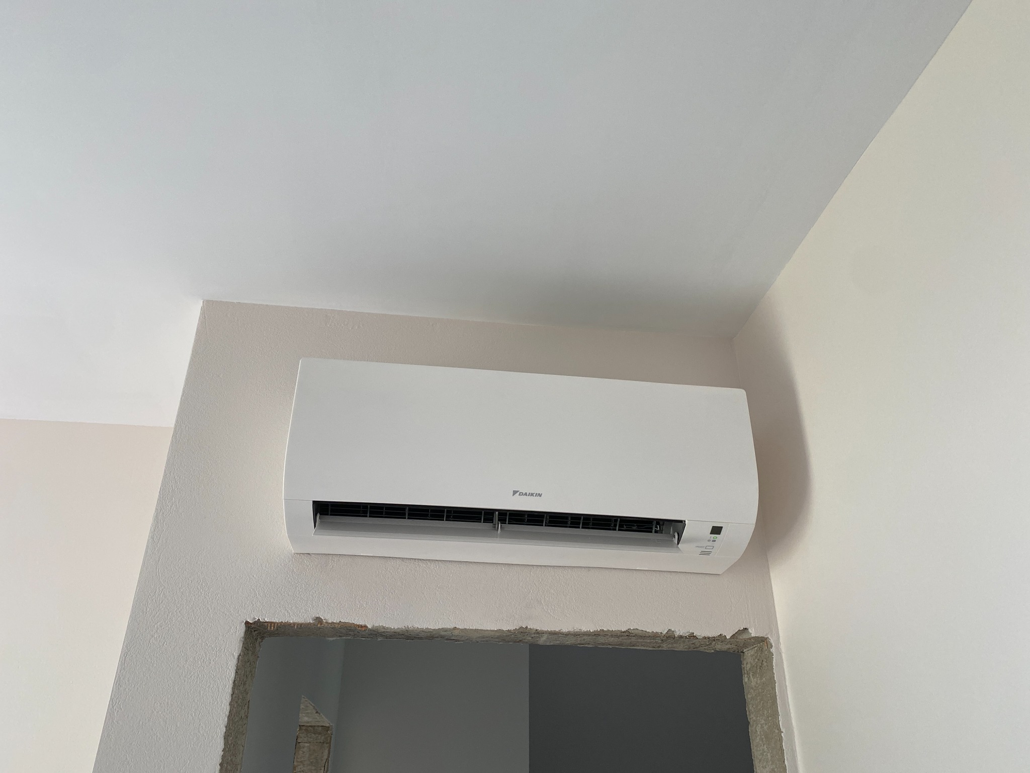 Biała klimatyzacja Daikin zamontowana na ścianie nad otworem w ścianie, w trakcie remontu. Widoczne niedoskonałości wykończenia.