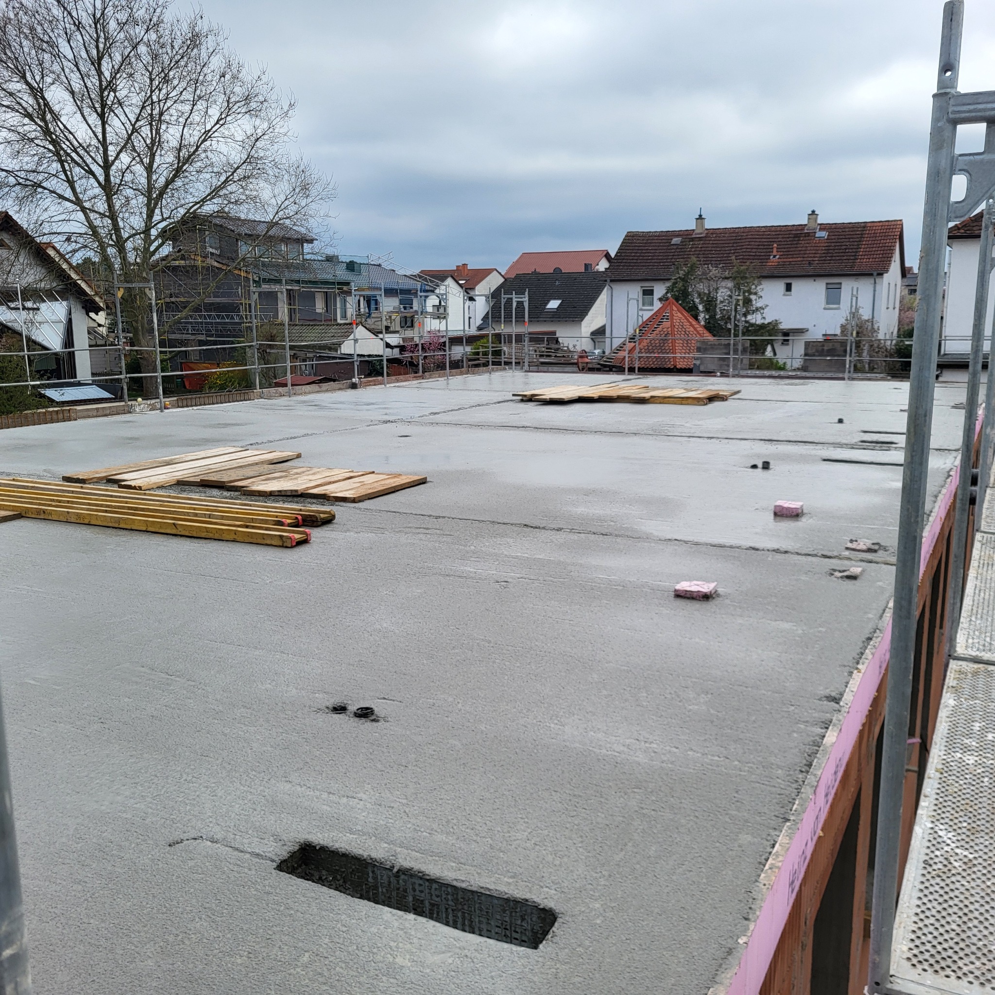 Świeżo wylany, mokry fundament pod budowę domu w Inowrocławiu, z widocznymi deskami szalunkowymi i elementami konstrukcyjnymi, sfotografowany w pochmurny dzień.