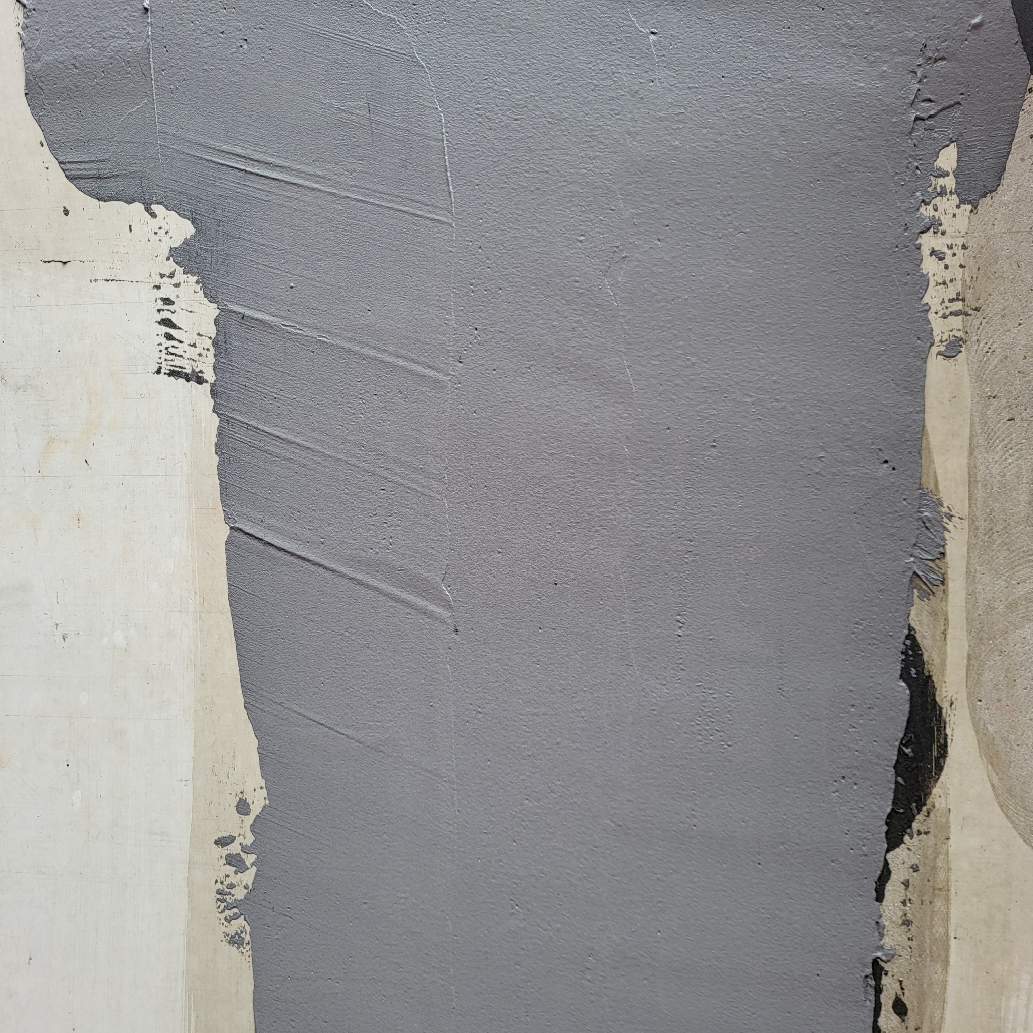 Fragment ściany z nałożoną szarą warstwą świeżego tynku, widoczne ślady po pacy, nierównomierne pokrycie w narożnikach.