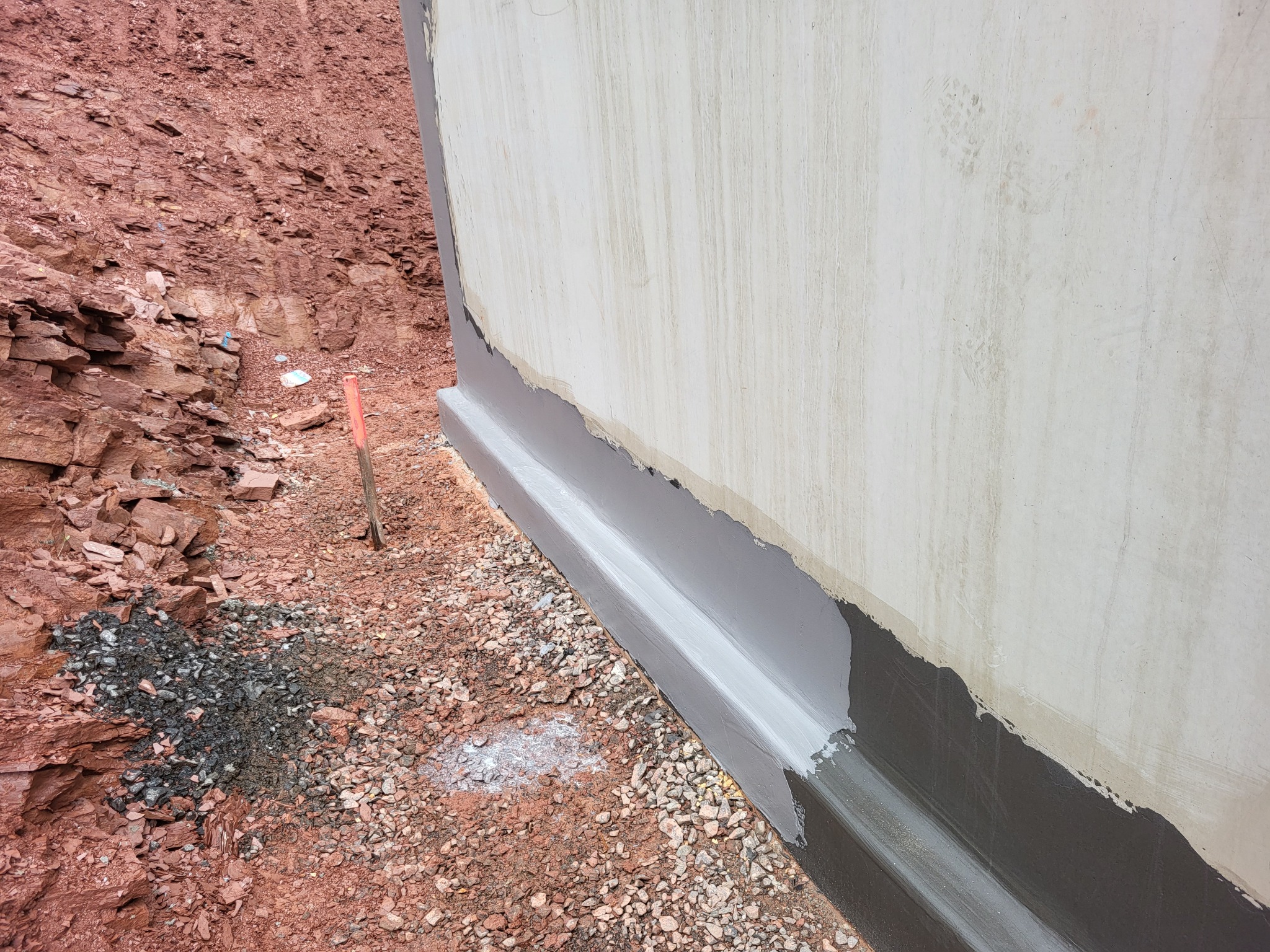 Świeżo zaizolowany fundament budynku z widoczną hydroizolacją i ociepleniem, częściowo zasypany ziemią i gruzem.