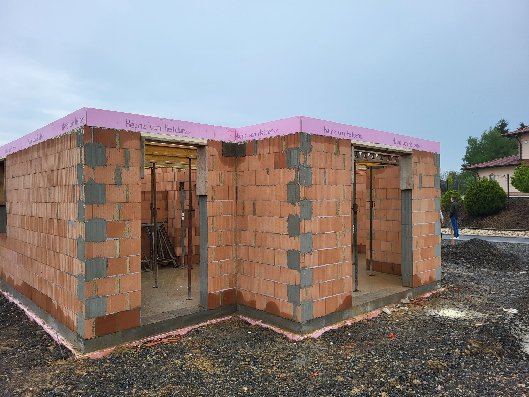 Wznoszone ściany domu z czerwonej cegły ceramicznej z widocznym szalunkiem i izolacją przeciwwilgociową, na zewnątrz rozsypany gruz.