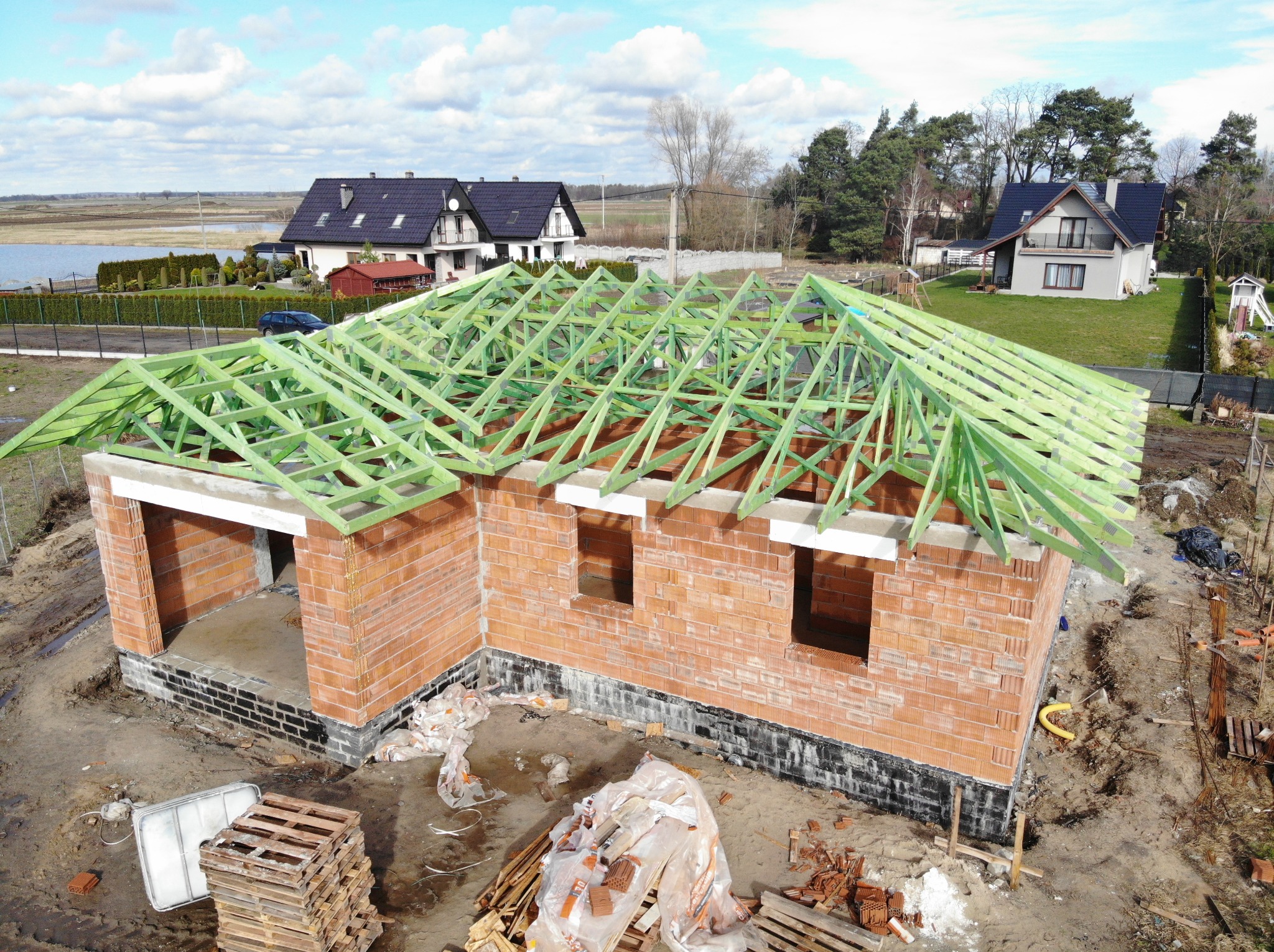 Wznoszenie muru z czerwonej cegły z zieloną konstrukcją dachu na budowie domu jednorodzinnego w słoneczny dzień.