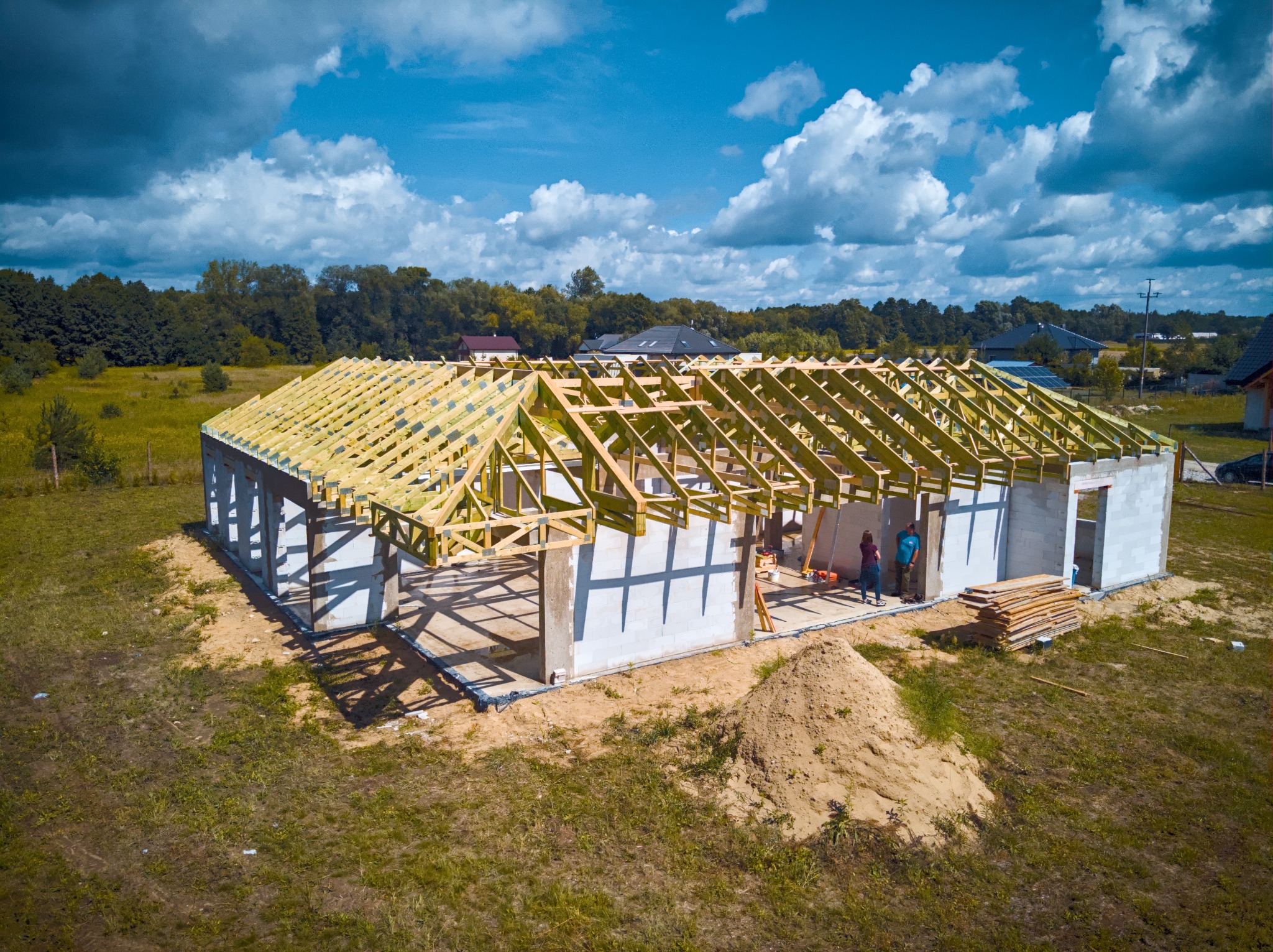 Budowa domu z betonu komórkowego z drewnianą konstrukcją dachu w trakcie montażu, widok z lotu ptaka, dwie osoby wewnątrz budynku.