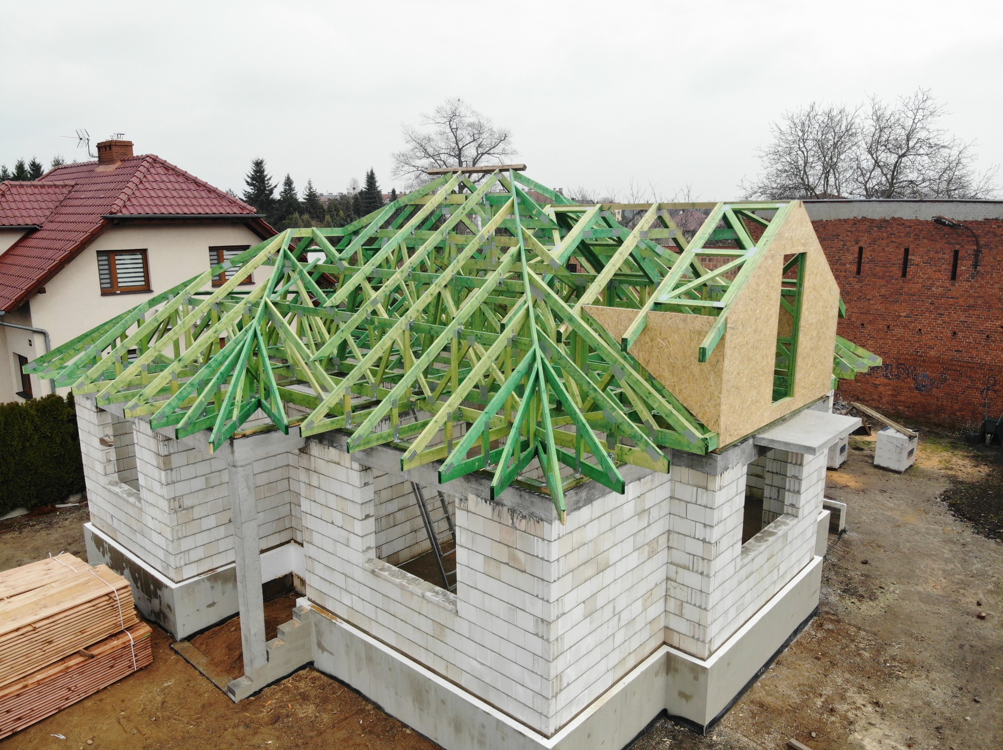 Wznoszenie domu z bloczków betonowych z konstrukcją więźby dachowej impregnowanej na zielono; widok z góry na budowę w trakcie realizacji.