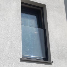 PLANETA SZKŁA SPÓŁKA Z OGRANICZONĄ ODPOWIEDZIALNOŚCIĄ - Nowo zamontowane okno z czarną ramą, zabezpieczone folią ochronną, w elewacji budynku o jasnej, chropowatej fakturze.