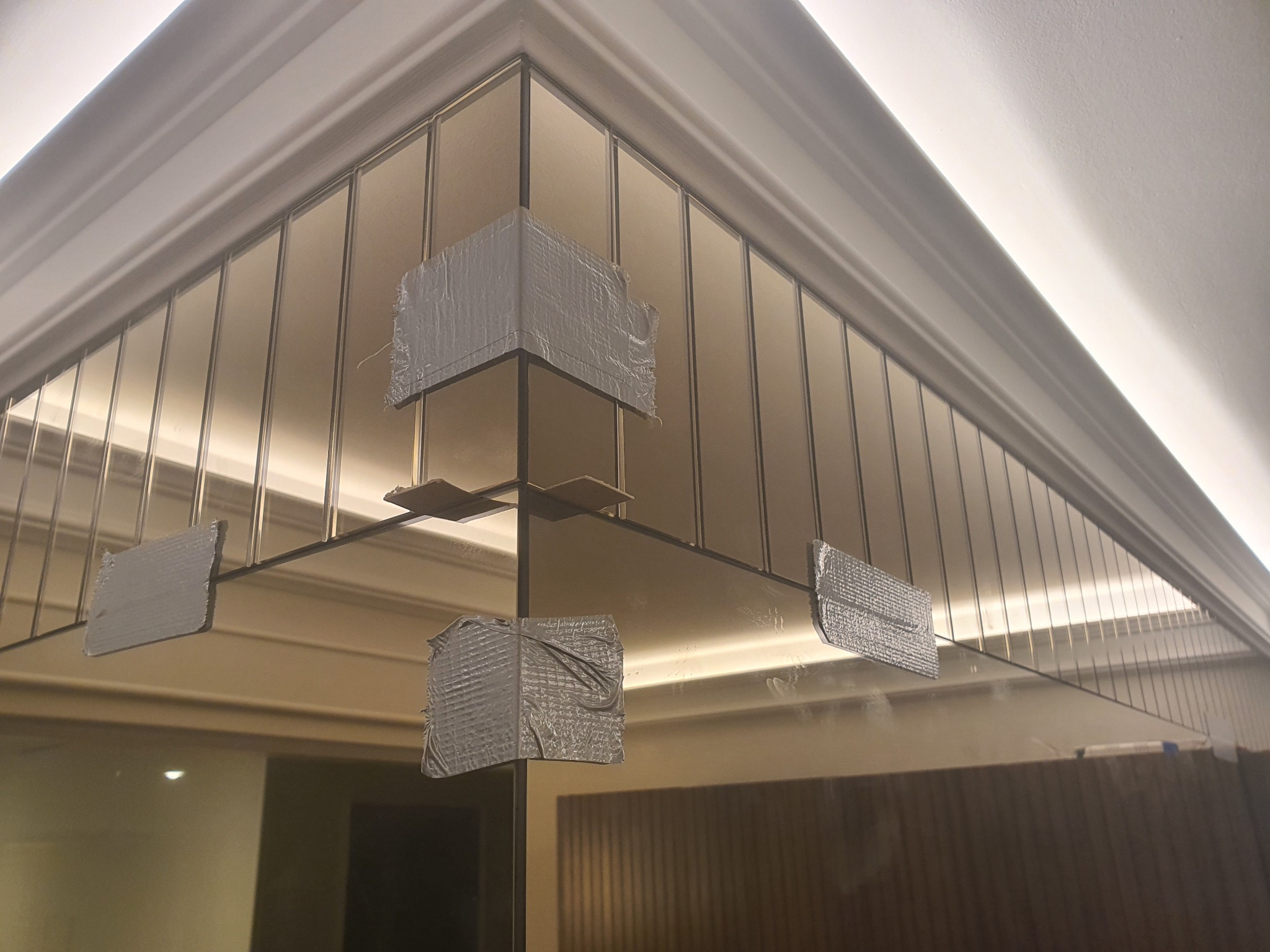 Szklana ściana działowa zabezpieczona taśmą montażową podczas instalacji w rogu pomieszczenia z oświetleniem sufitowym.