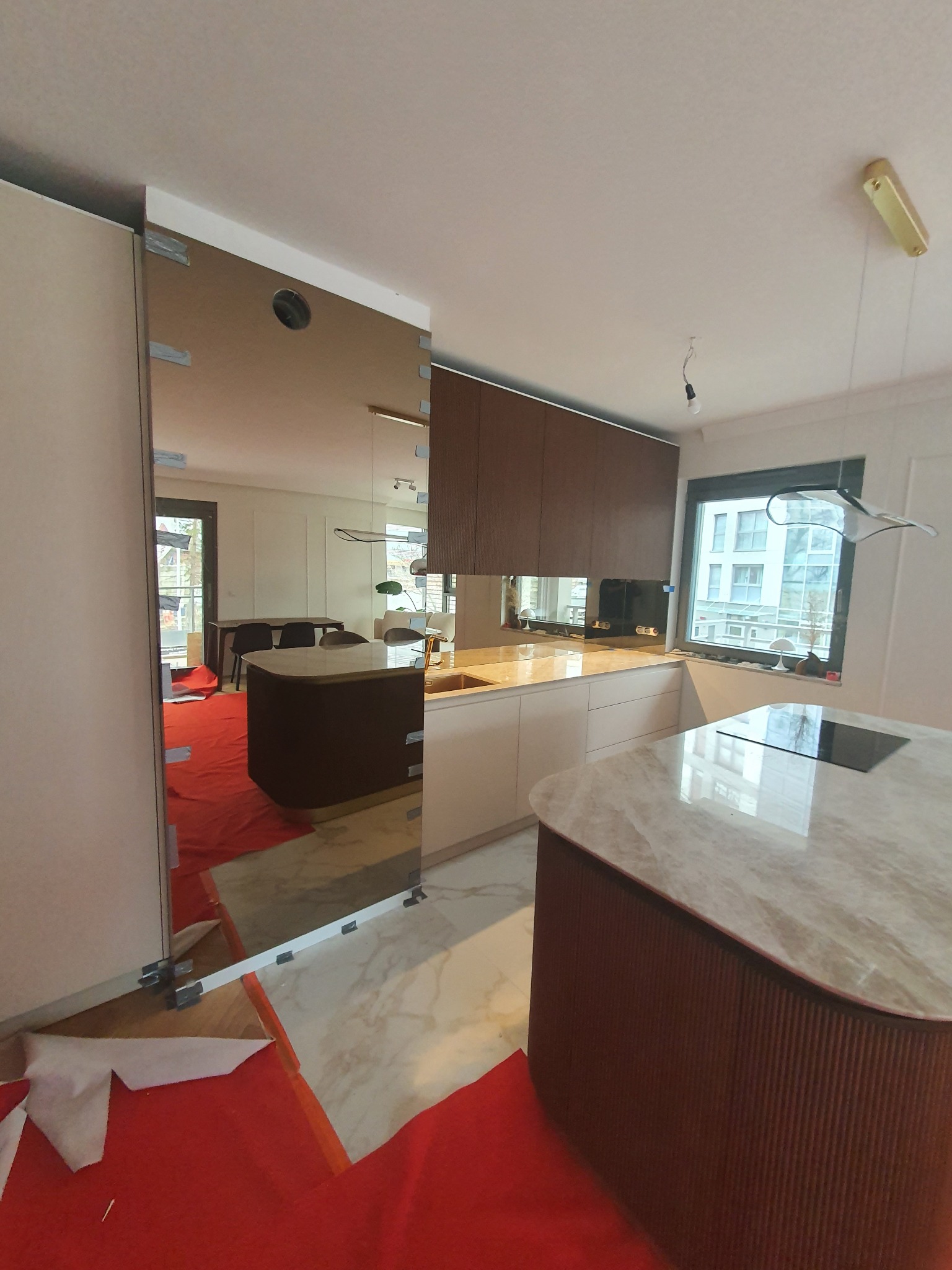 Montaż lustrzanej ściany w kuchni, widoczne zabezpieczenia podłogi folią ochronną i mocowania szkła.