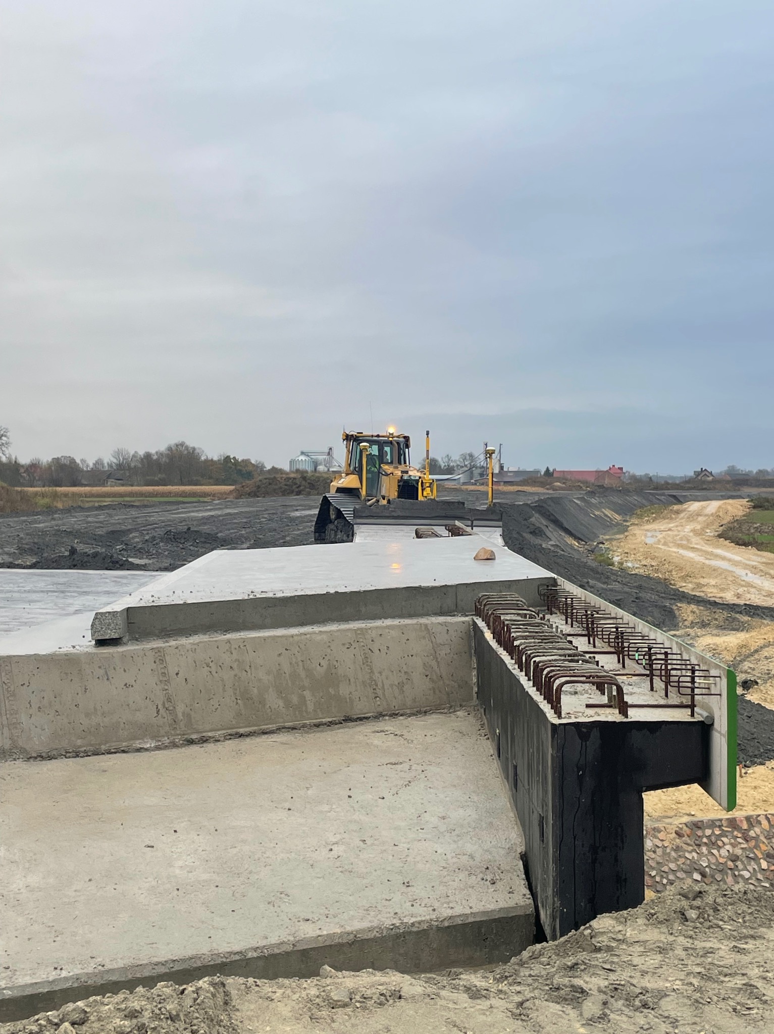 Żółty spychacz na betonowej konstrukcji w Tarnowie, z widocznymi zbrojeniami i przygotowanym terenem pod budowę drogi.
