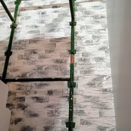 Artur Konieczny - Ściana wykończona dekoracyjną, szarą cegłą, widoczna z perspektywy rusztowania w trakcie prac wykończeniowych.