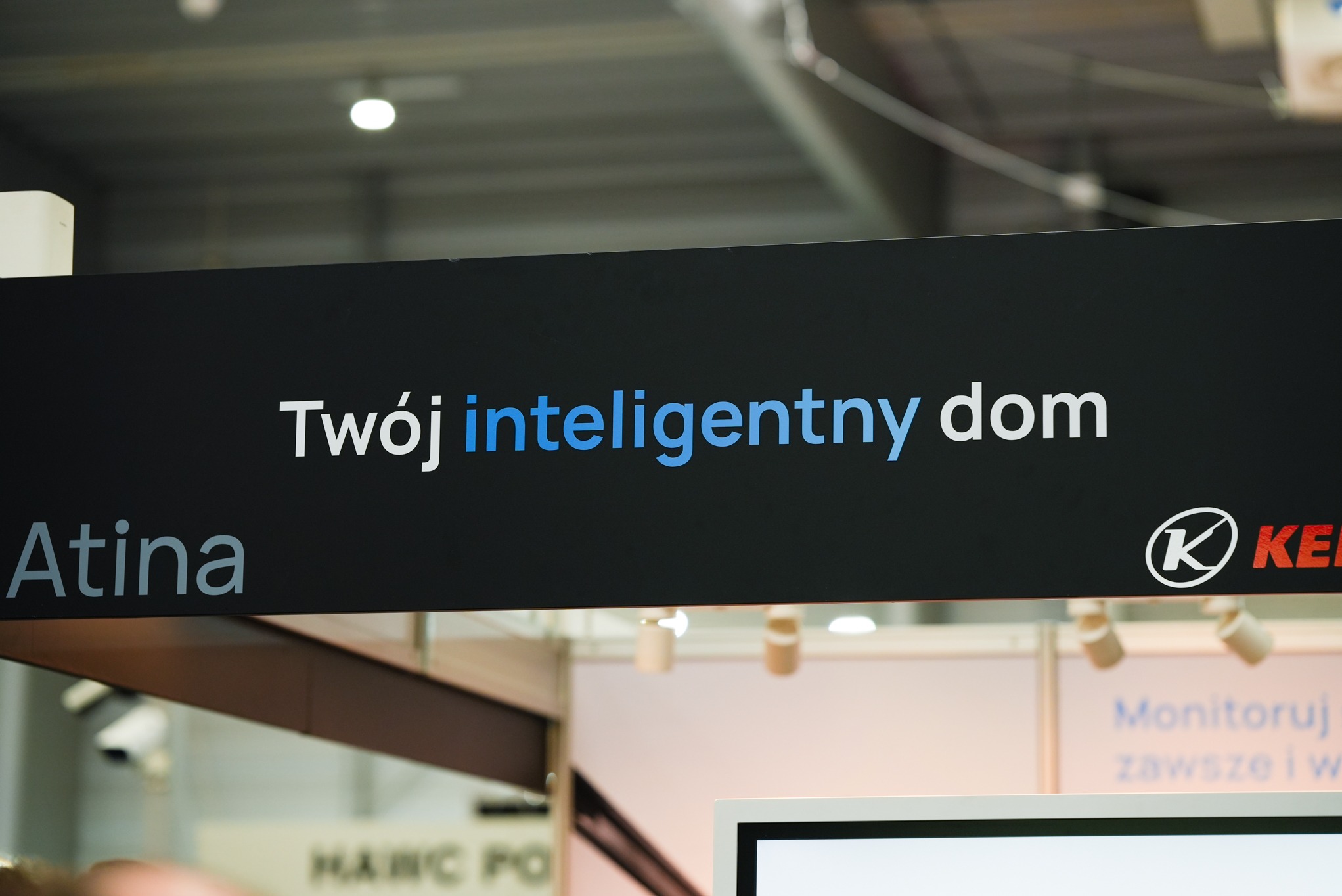 Ekspozycja targowa firmy Atina prezentująca hasło 'Twój inteligentny dom' z logo firmy w prawym rogu, na tle widoczne elementy stoiska i oświetlenie.