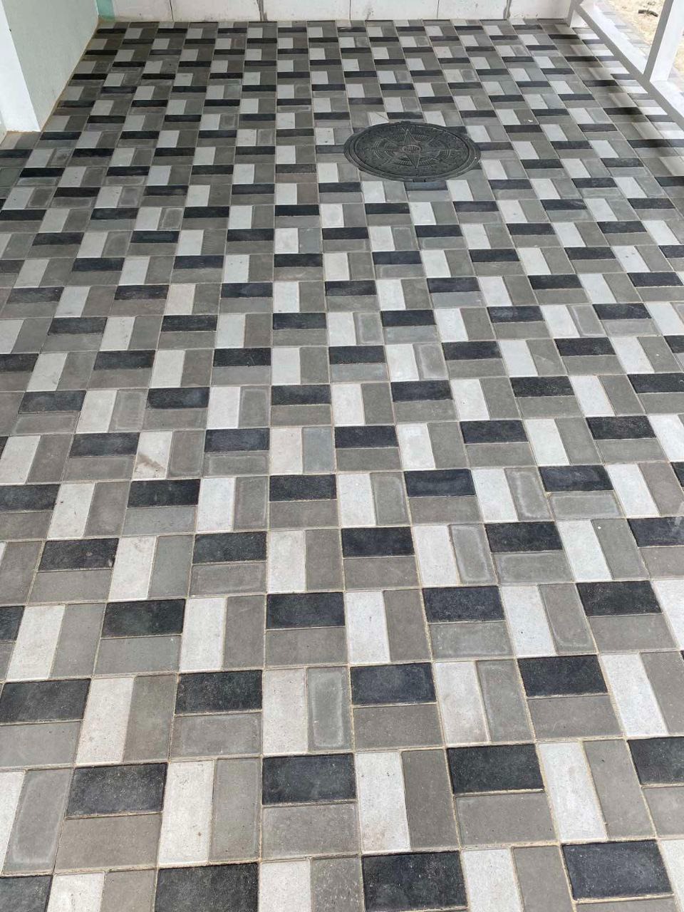 Ułożona nawierzchnia z kostki w odcieniach szarości i czerni, z okrągłą studzienką kanalizacyjną pośrodku, widok z góry.