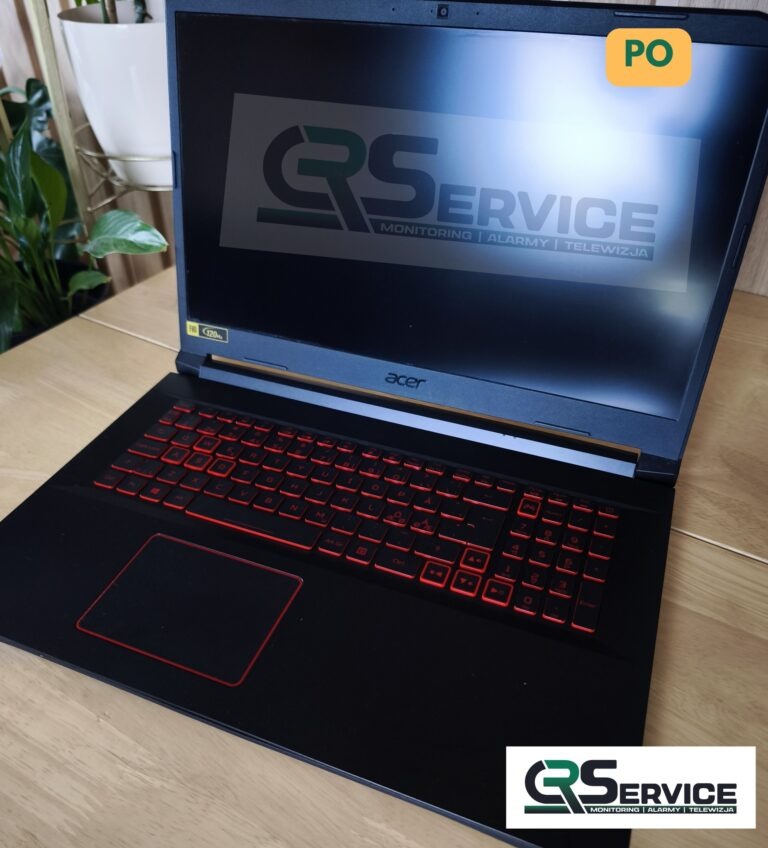 Czarny laptop Acer z podświetlaną na czerwono klawiaturą, na ekranie logo firmy z branży monitoringu, alarmów i telewizji. Widoczne biurko i roślina w tle.