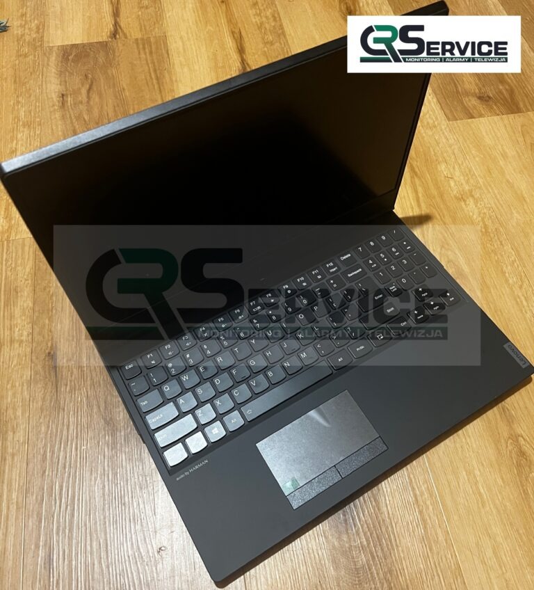 Czarny laptop Lenovo z widoczną klawiaturą i touchpadem, leżący na drewnianej podłodze. Widoczny logotyp firmy QService w tle i w prawym górnym rogu.